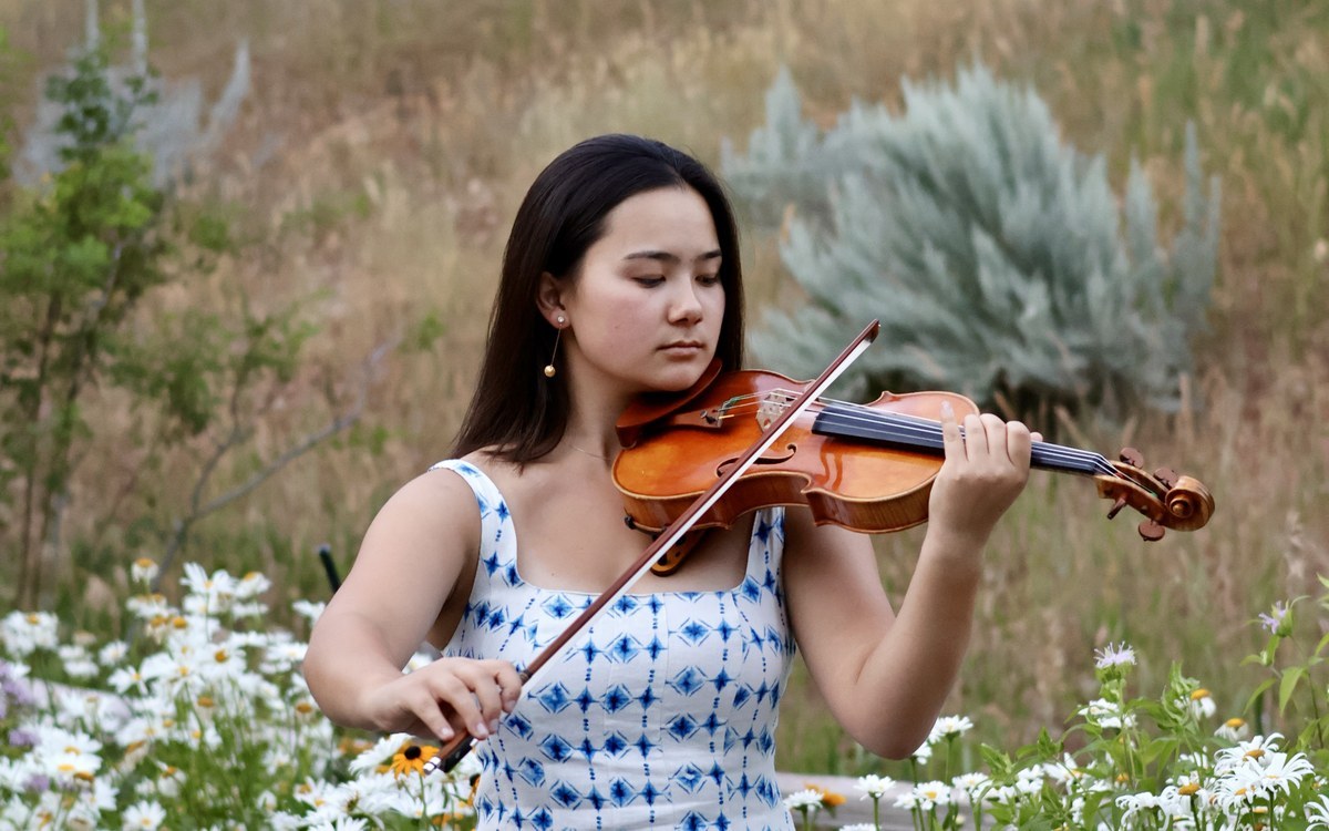 A violinist playing outdoors in a wildflower meadow.