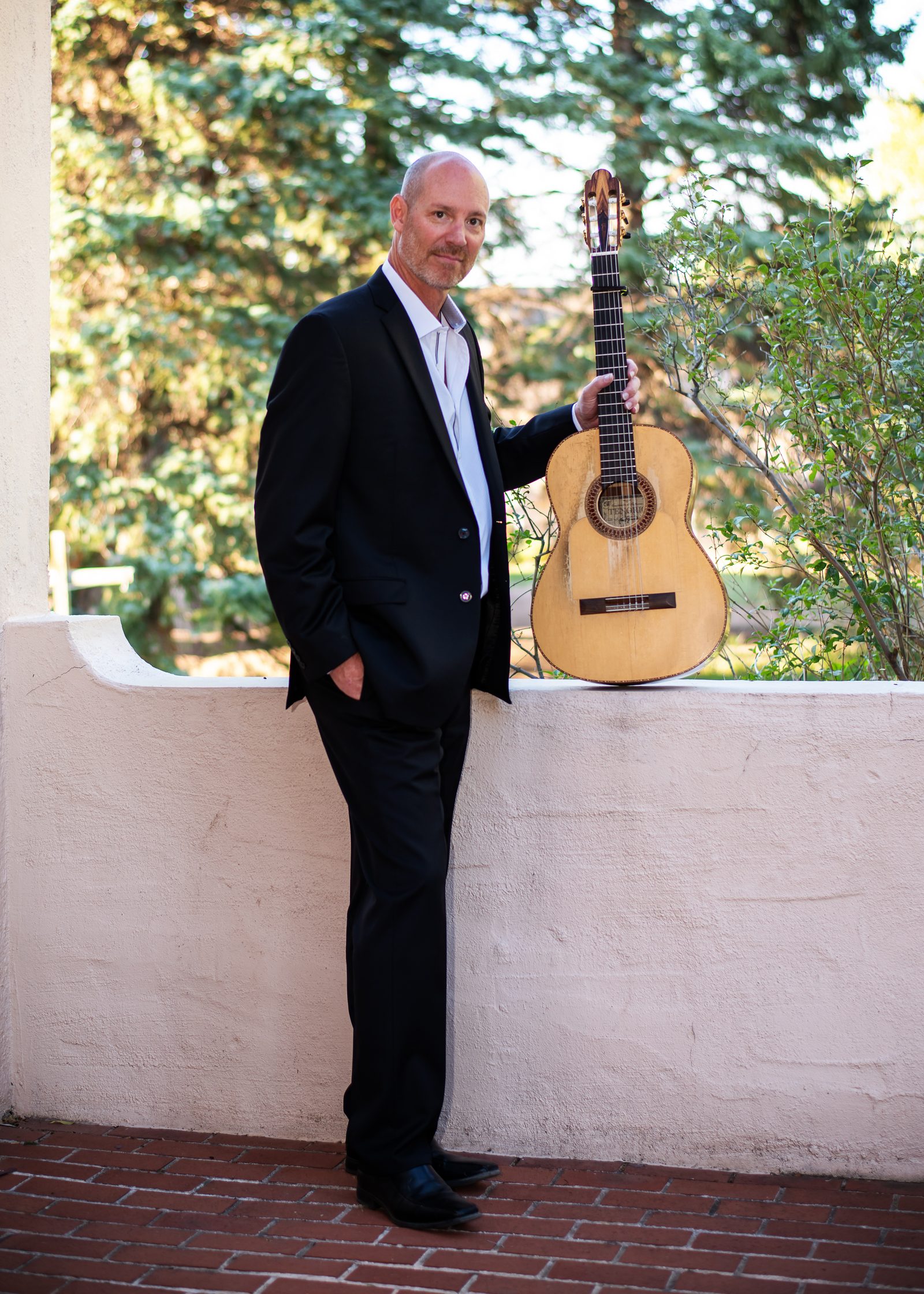 Gary Meyers in a suit with his guitar on a garden wall.