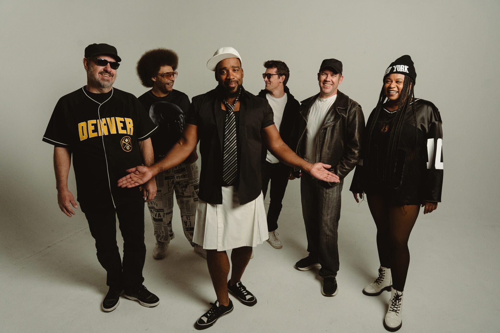 The band in black Denver baseball jerseys in a studio, arms out.