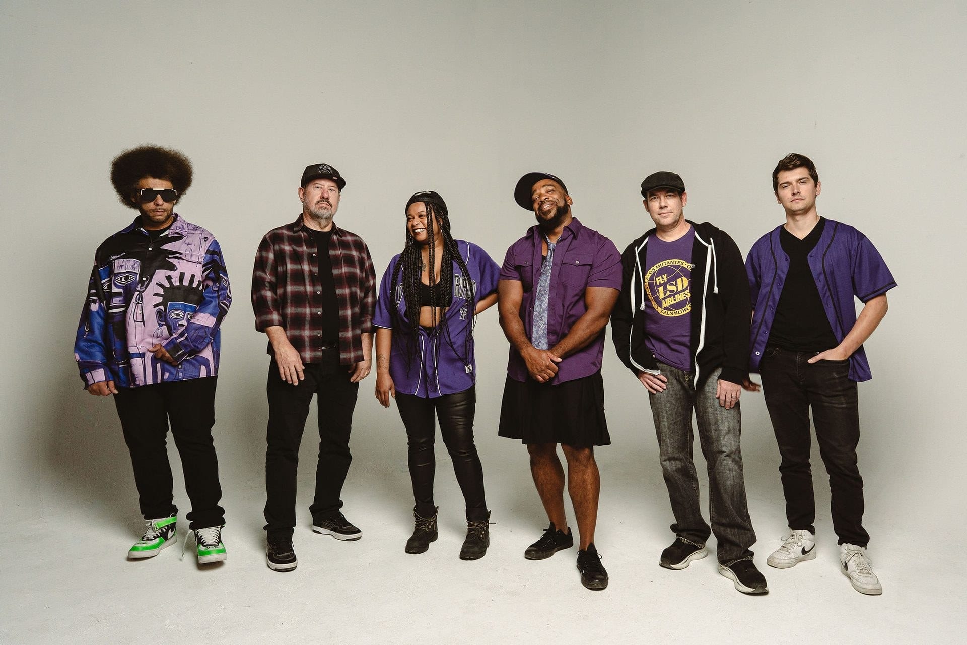 The band lined up in purple against a white studio wall.