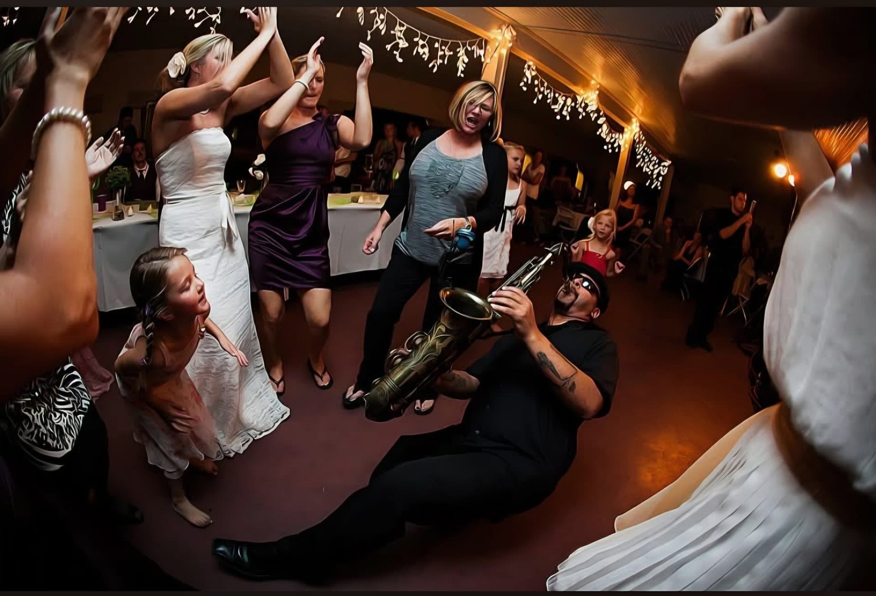 A saxophonist playing on a wedding dance floor with the guests dancing around the horn.