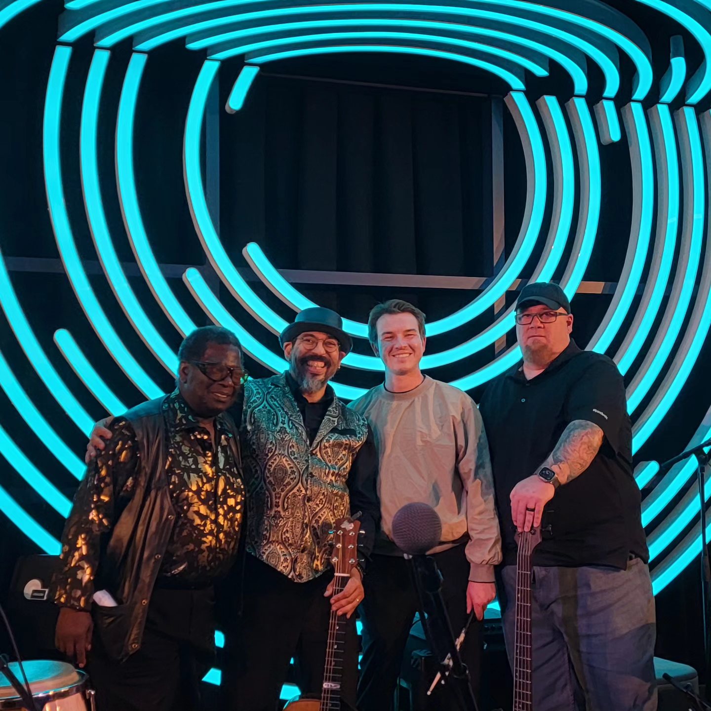 Tony Medina and three other players on a stage lit with teal neon.