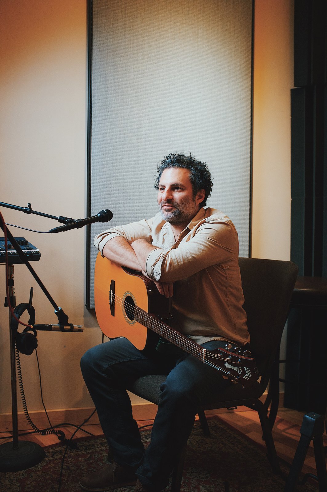 René Moffatt seated with an acoustic guitar beside a studio microphone.