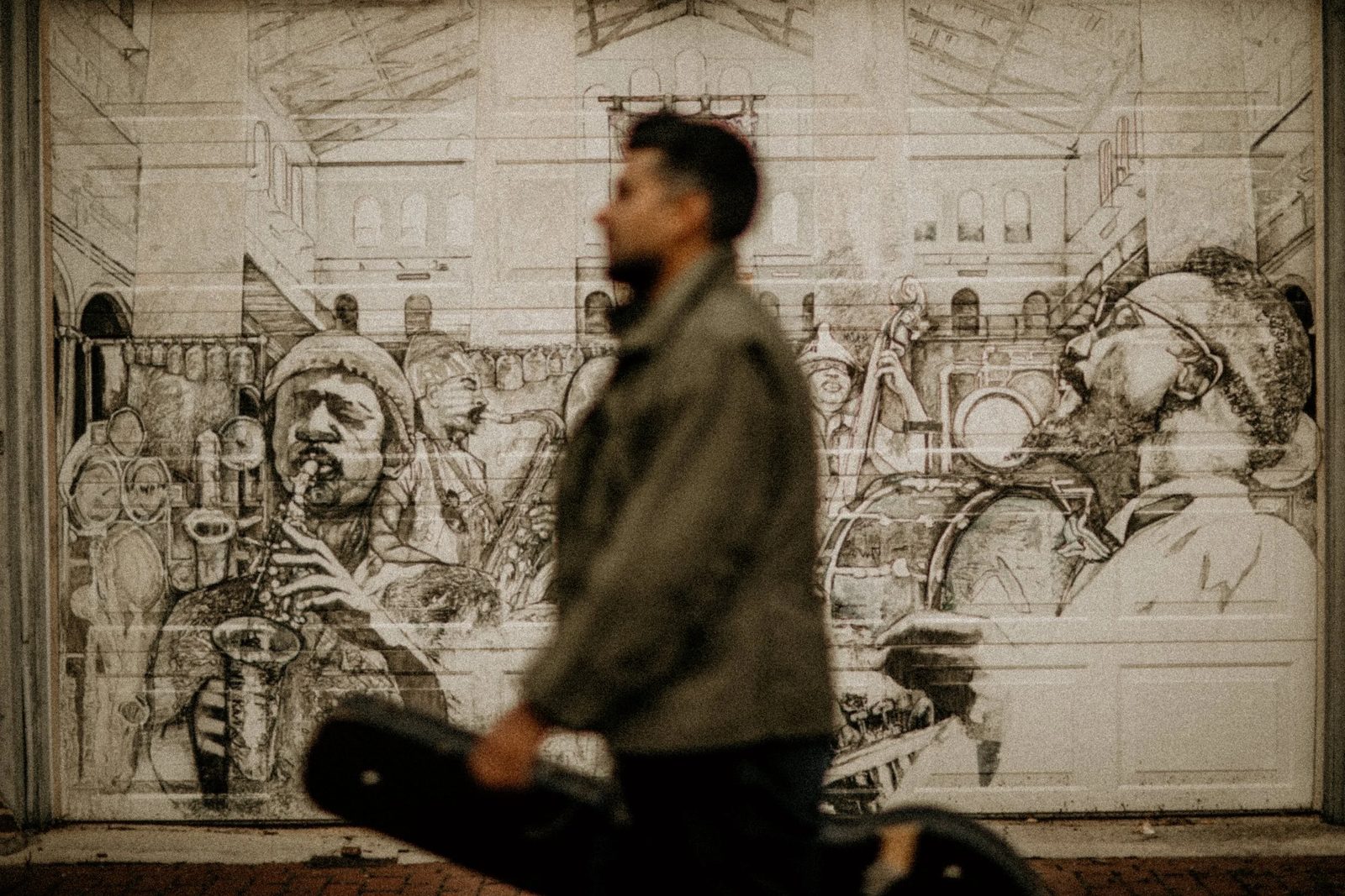 Tejas Singh carrying a guitar case past a jazz mural.