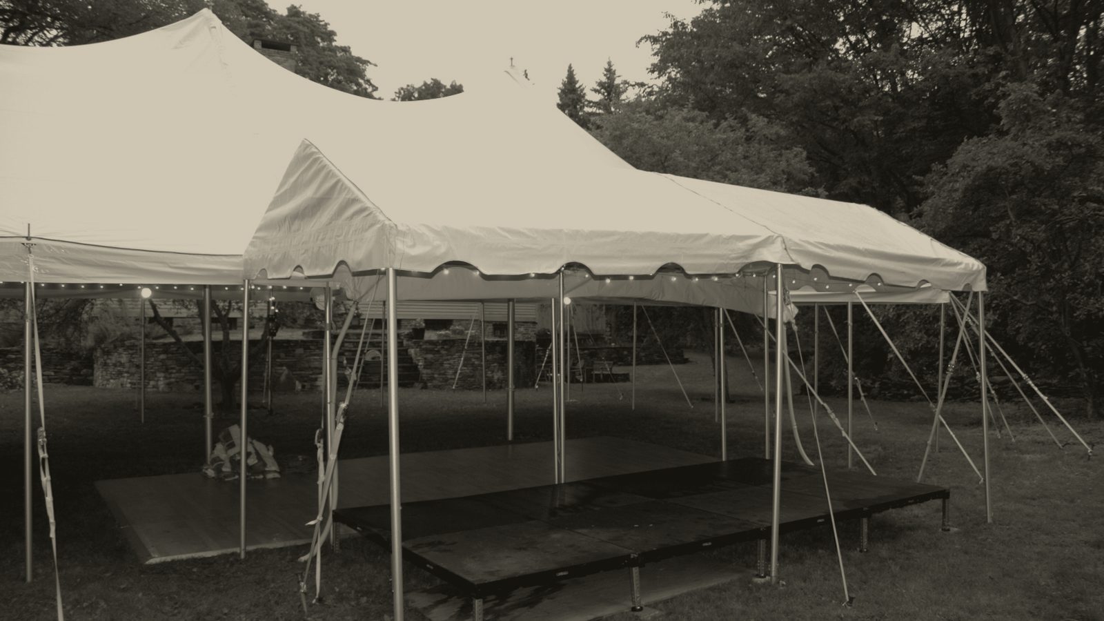A frame tent on grass with a plywood stage deck under it.