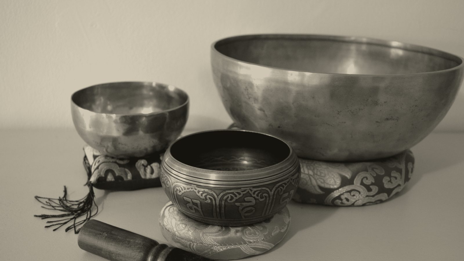 Three singing bowls on cushions with a mallet beside them.