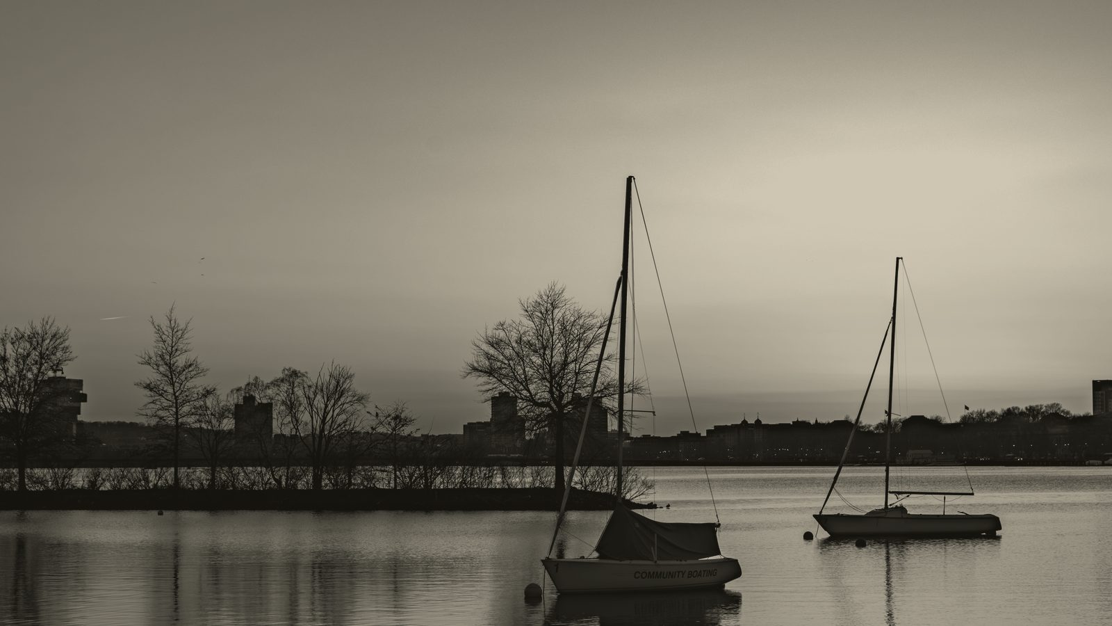 Two sailboats moored on still water at sunset.